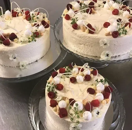 Tre vita tårtor med hallon, maränger och ätbara blommor på glasfat